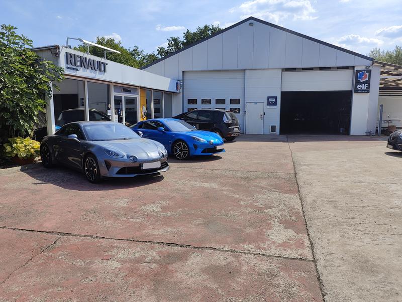 Het gebouw van Garage Bogaerts in Tremelo: de Renault-toonzaal en de werkplaats met de borden van Dacia en elf, met vooraan een grijze en een blauwe Alpine A110 en daarachter een donkere Renault