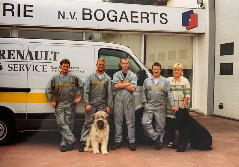 Oude foto van een afdruk: vier mechaniekers in grijze overalls en een vrouw staan met twee honden, een lichte en een zwarte, voor een witte Renault-servicebestelwagen van Garage Bogaerts, onder het uithangbord N.V. Bogaerts